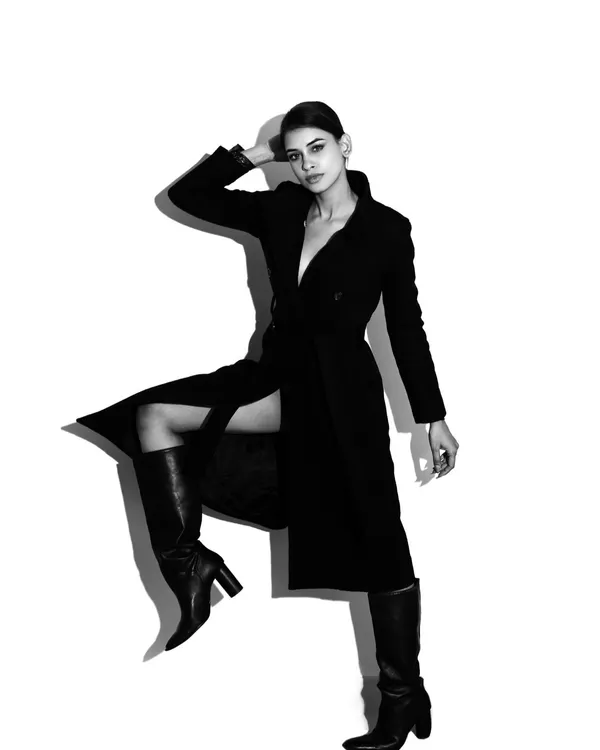 A dynamic full-length studio portrait in black and white. The high-contrast lighting and strong pose create a powerful fashion image that emphasizes the silhouette and attitude.
