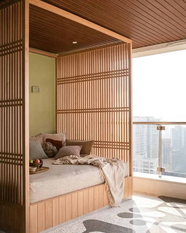 This cozy daybed, framed in wood and nestled in a high-rise balcony, creates the perfect spot for an afternoon siesta with a view of the Mumbai cityscape.