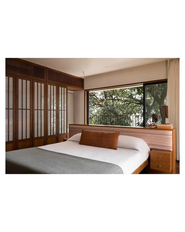 This master bedroom is designed for tranquility, with a low island bed and Japanese-inspired shoji screen wardrobes. The large window frames a perfect view of the trees, creating a zen-like space for sleep and relaxation.