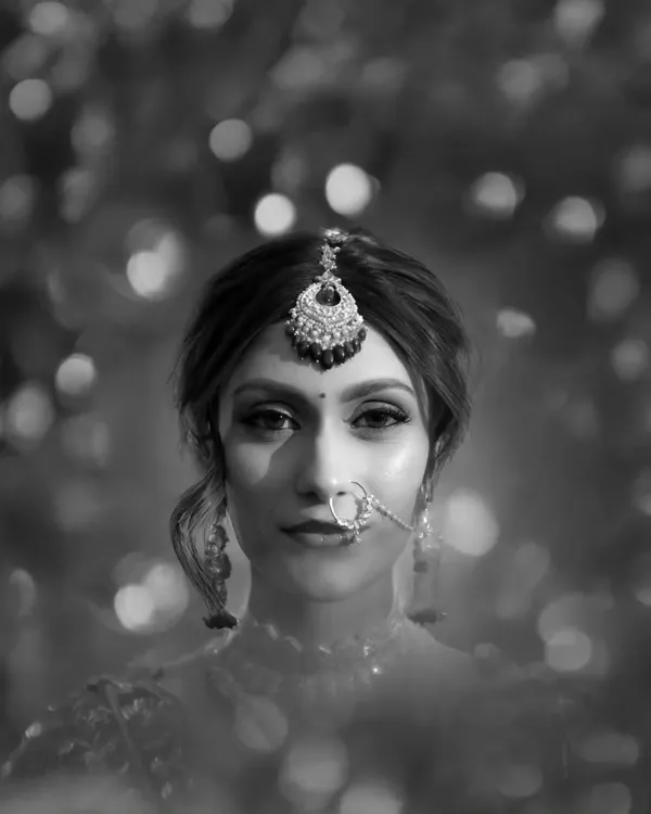 A stunning black and white bridal portrait, with a dreamy, bokeh background that makes her expressive eyes and intricate jewelry the focus.