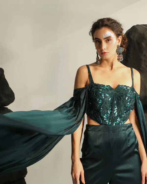 A breathtaking shot from an occasion wear campaign, capturing the dramatic flair of an emerald green embellished top with flowing sleeves. The styling and pose create a sense of movement and high drama.