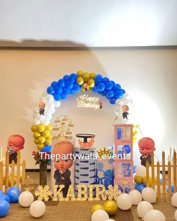 A classic Boss Baby theme for a first birthday. This setup features a 'Happy Birthday' neon sign, character cutouts, and a blue, white, and gold color scheme.
