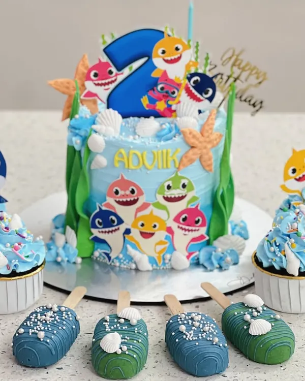 Doo doo doo! A fun Baby Shark themed set for a second birthday. I made a custom cake, matching cupcakes, and even themed cakesicles to create a complete dessert table.