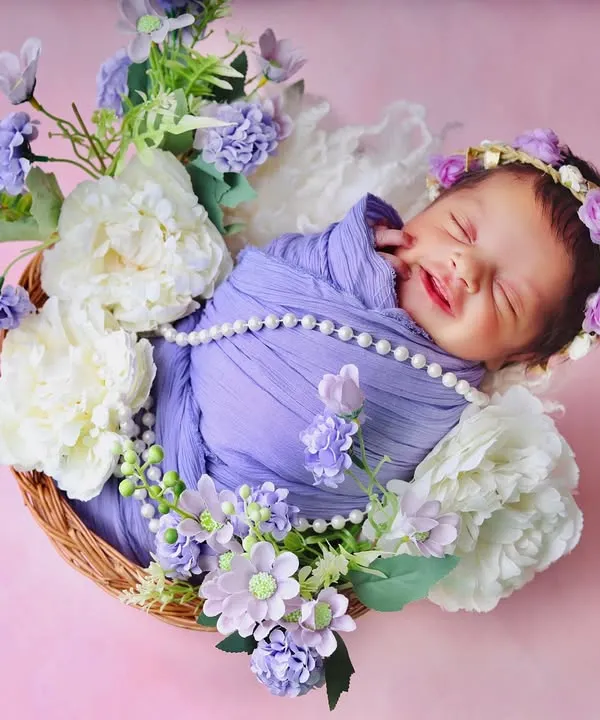 A perfect, happy smile from a sleeping newborn, nestled in a basket of soft white and purple flowers. This is the kind of pure, peaceful moment I love to capture.