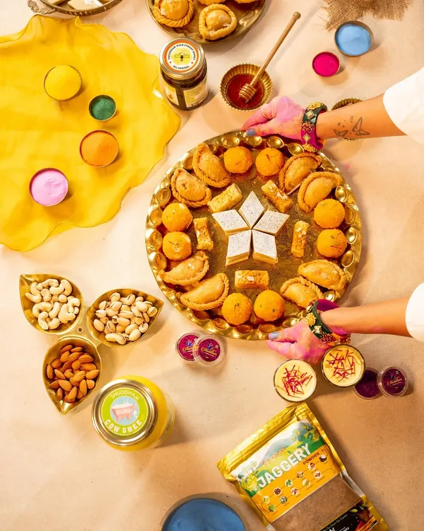 A vibrant flatlay of Holi essentials, from colorful powders to traditional sweets and nuts. This top-down shot captures the festive preparation and abundance, perfect for a brand's Holi campaign visuals.