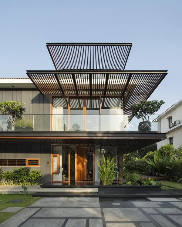 The front elevation of Villa re:FORM, showcasing a layered composition of slatted pergolas, a glass-railed balcony, and dark-clad lower volumes.