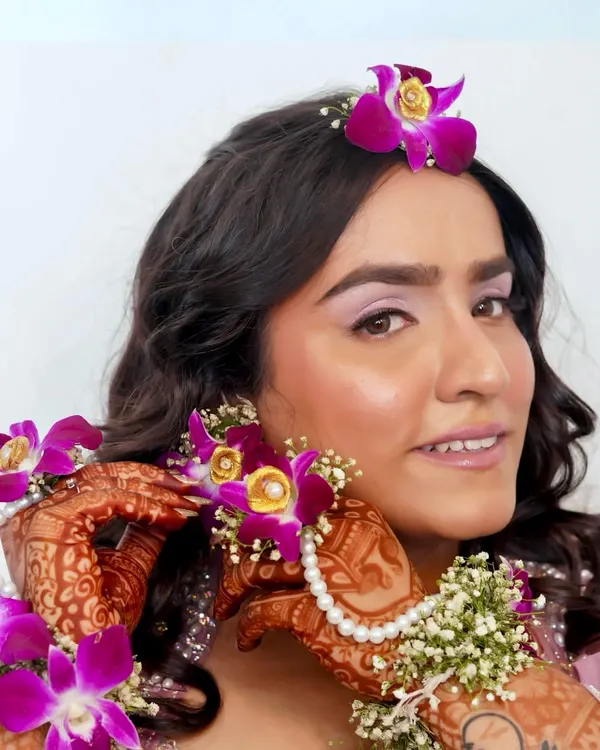 A close-up of a beautiful Haldi look. The makeup is subtle and elegant, with a soft lilac eyeshadow that picks up the color of the fresh orchids in her hair and jewellery.