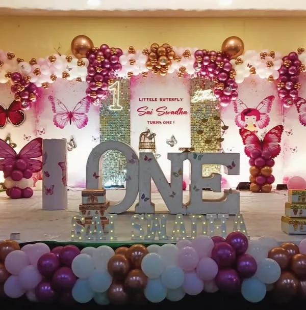 This was an unforgettable first birthday celebration with an enchanting butterfly theme. I designed a full stage setup featuring large 'ONE' marquee letters, intricate balloon arrangements in pinks and whites, and beautiful butterfly details throughout. It's all about creating a grand and memorable first milestone.