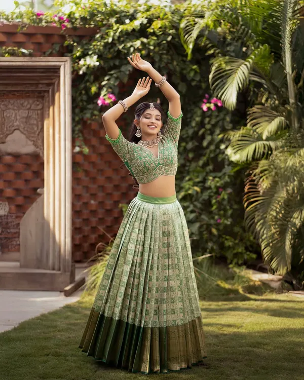A joyful and vibrant Kanchi Pattu half saree in a refreshing pista green. The pleated lehenga creates a beautiful, full circle when twirling, and the look is completed with a heavily hand-embroidered crop top style blouse.