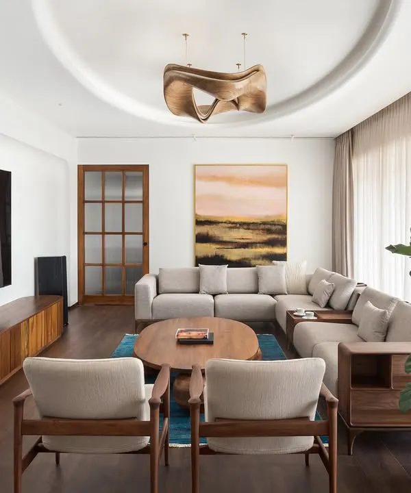 This view of the West Coast Residence shows how we balance different elements. The large sectional sofa provides comfort, while the sculptural coffee table and statement wooden ceiling light add layers of artistic expression to the living area.
