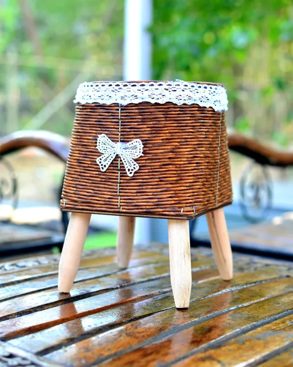 A chic, square-shaped woven planter on wooden tripod legs, perfect for a bohemian or rustic decor style.