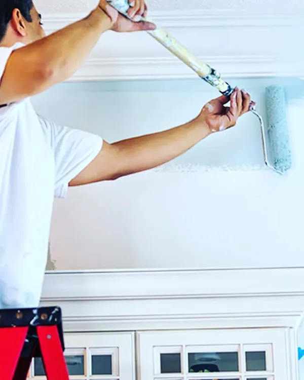 A painter using a roller with an extension pole to apply an even coat of paint near the ceiling. Using the right tools ensures a smooth, consistent finish without drips or marks.