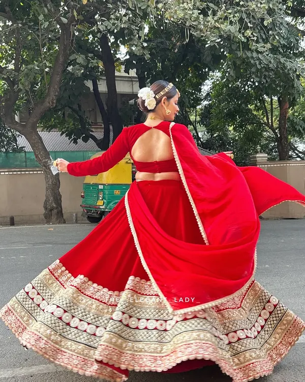 A full view of the stunning backless design and the beautiful flare of my red velvet bridal lehenga. The wide, embroidered border adds weight and grandeur, making it perfect for those classic twirling shots.