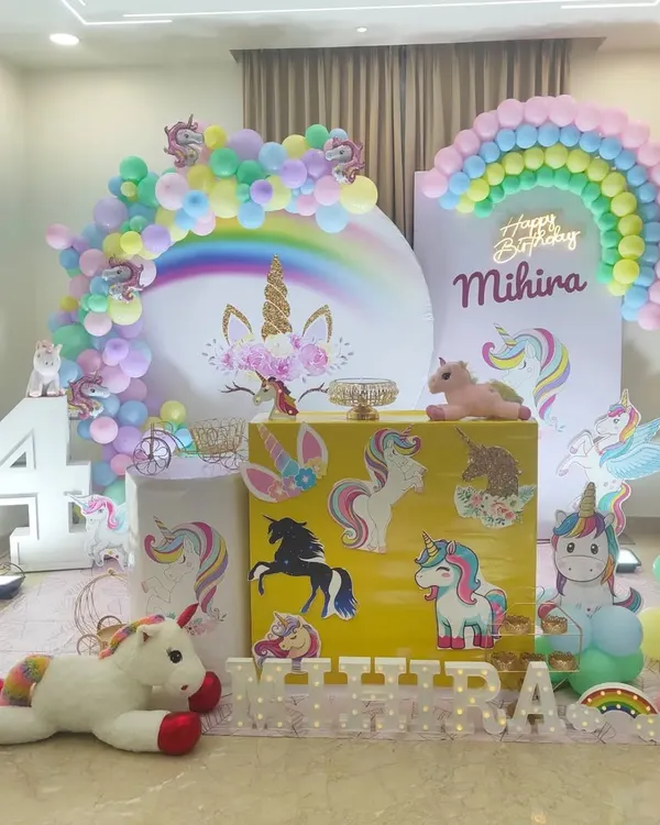 A complete unicorn and rainbow party setup with multiple unicorn props, a pastel rainbow balloon arch, and a large circular backdrop.