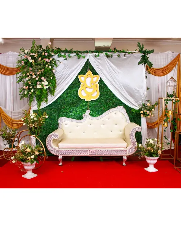This elegant baby shower setup features a lush green grass wall as the backdrop. I used white and gold drapes, a Ganesha cutout, and floral arrangements on props like a decorative tricycle to complete the look.
