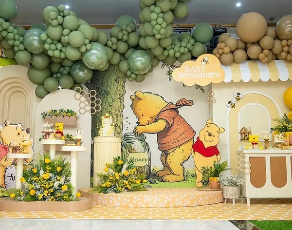 A complete Winnie the Pooh themed baby shower stage, featuring a honey pot cake stand, character cutouts, and a balloon tree. The entire setup is designed to look like a scene from the Hundred Acre Wood.