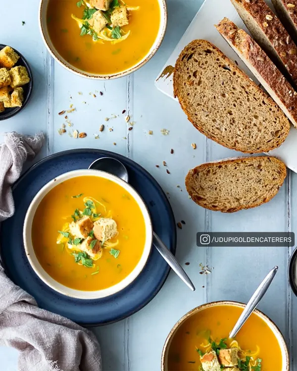 A comforting bowl of our creamy pumpkin soup, garnished with croutons and fresh herbs, and served with slices of multigrain bread. A wholesome start to any meal.