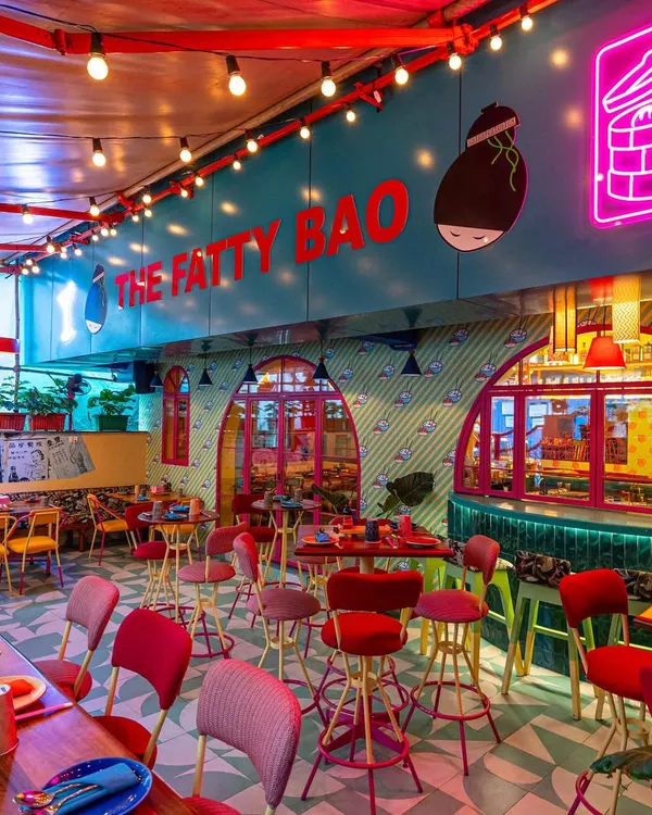 A wide shot of The Fatty Bao's interior, capturing the playful chaos of neon signs, colorful furniture, and graphic wall art. This type of image is perfect for showing customers the fun and lively atmosphere they can expect.