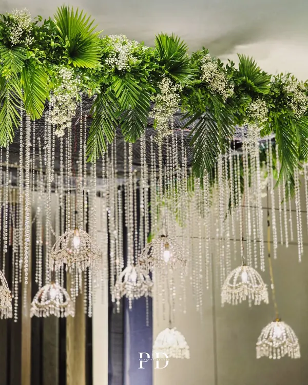 The canopy of a crystal entrance, showing how we blend lush greenery like palm fronds with delicate baby's breath and sparkling crystal strings for a look of modern opulence.