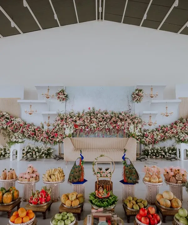 A wide shot showcasing the breathtaking decor of a naming ceremony. The stage is adorned with cascading flowers and traditional fruit offerings, setting a beautiful scene for the day's events.