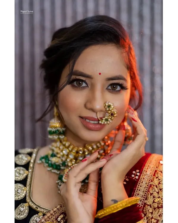 A stunning close-up bridal portrait. The focus is on the bride's flawless makeup, intricate nose ring (nath), and sparkling eyes, capturing the beauty and excitement of her special day.