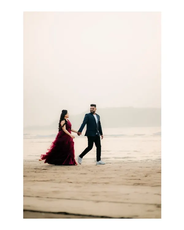 A classic pre-wedding photo of a couple walking hand-in-hand on the sand, with the bride's gown flowing beautifully.