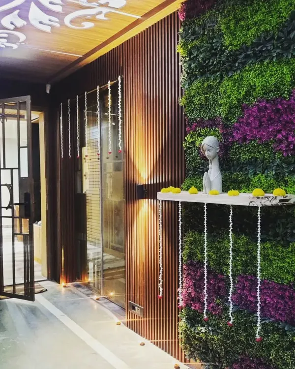 A view of an elegant entryway we designed, combining a vibrant artificial green wall with rich wood louvers. The integrated shelf and warm lighting create a welcoming focal point in this modern home.