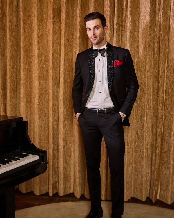 A classic black tuxedo is elevated with textured, patterned lapels and a sharp bow tie. The red pocket square adds a pop of color, making this a perfect ensemble for a sophisticated evening affair or cocktail event.