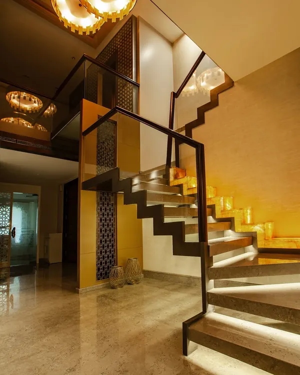 A modern floating staircase with stone treads and ambient under-step lighting, framed by sleek glass and wood railings. The classic trellis pattern in the backdrop adds a timeless touch to this contemporary design.