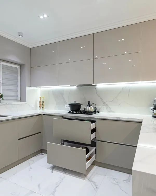 This is the heart of a modern home, a minimalist kitchen designed for maximum function. We used a high-gloss laminate finish in a calming neutral tone, paired with a durable marble-patterned quartz countertop and backsplash. The handle-less drawers and cabinets create a seamless look, while the under-cabinet LED lighting provides perfect task illumination.