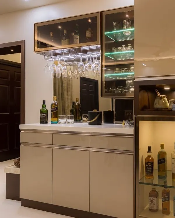 A compact and stylish bar and crockery unit. It features glass shelves with green backlighting, a rack for hanging wine glasses, and a dedicated lit-up section for premium bottles.