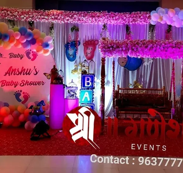 A modern baby shower decoration with a personalized backdrop for Dr. Baby Anshu. The setup includes a colorful balloon arch, a decorated swing, and light-up 'BABY' blocks.