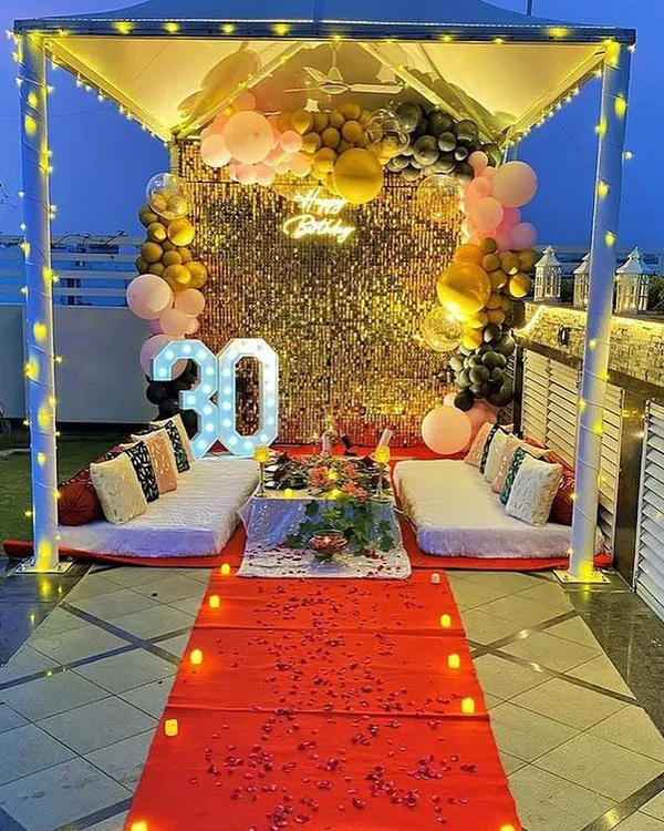 A luxurious cabana setup on a terrace for a 30th birthday celebration, complete with a red carpet entrance, low seating, a sequin backdrop, and a custom neon sign. This is perfect for milestone birthdays and grand romantic gestures.