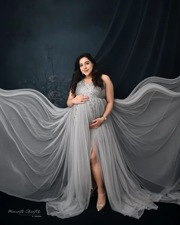 A vision in silver. This portrait uses a flowing grey gown and a dramatic fabric toss to create a sense of movement and ethereal beauty against a dark, moody backdrop.