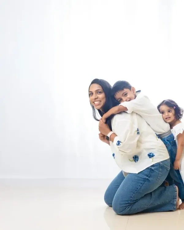 A mother and her children share a playful, loving moment against a clean, white background. This minimalist style allows their genuine emotions to be the focus of the photograph.