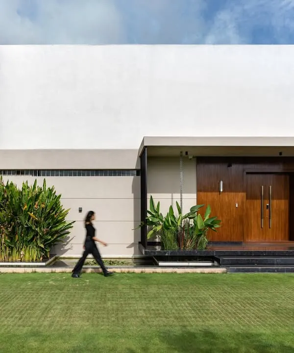 The entrance to the Celadon residence showcases a blend of clean white planes, warm wood cladding, and lush greenery. This facade sets the tone for a home where modern architecture meets the tranquility of nature.