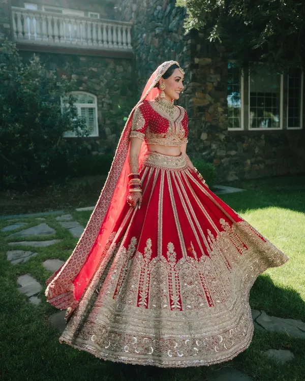 A stunning full-length portrait of the bride, Nita, in her traditional red and gold lehenga. The twirl of the skirt shows off the magnificent craftsmanship of her attire.