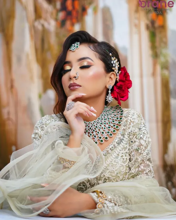 A beautiful modern glam look featuring golden cut-crease eyeshadow, a bold red flower in the hair, and a stunning diamond and emerald necklace.