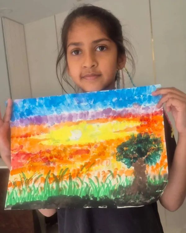 A young student, Krishika, proudly displays her sunset landscape created using a finger painting technique. This method is a fun, tactile way for children to learn about color blending.