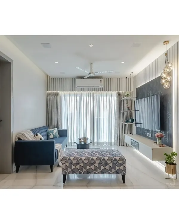This living room captures my signature style: clean, modern, and comfortable. I used vertical fluted panels and integrated LED lighting to add texture and height to the space, while the floating TV unit keeps the floor clear and creates an airy feel. The pop of blue in the sofa and the geometric ottoman bring personality into the neutral palette.