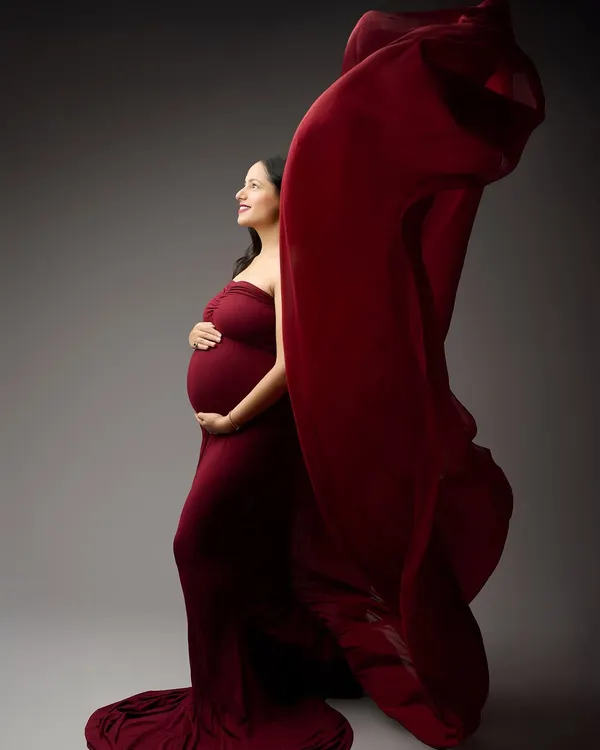 Capturing the beauty of movement, this shot features a vibrant red gown with a flowing train against a classic grey backdrop. This technique adds a dynamic and artistic flair to the maternity portrait.