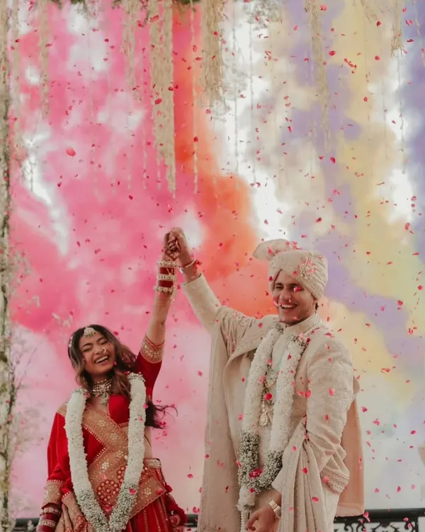 A moment of pure celebration for the newly married couple. The groom is radiant in our classic ivory sherwani, featuring subtle all-over embroidery that perfectly complements the festive atmosphere.
