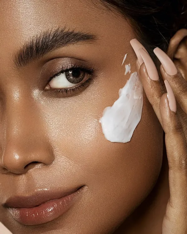 A macro shot demonstrating the application of a rich face cream. The focus is on the luxurious texture of the product against the model's radiant skin, emphasizing a moment of gentle self-care. The composition draws the eye to the interaction between the hand and face, creating an intimate feel.