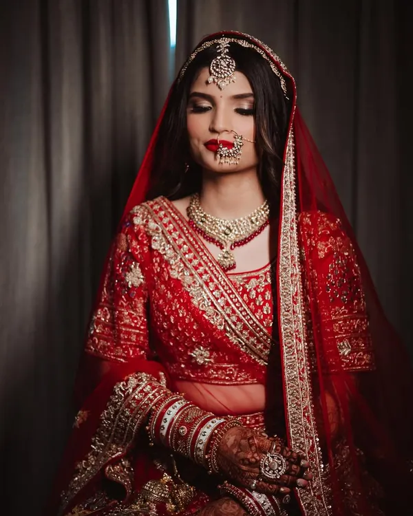 A moment of serene beauty before she says 'I do'. This classic red bridal look, complete with a bold lip and traditional jewelry, is the epitome of timeless elegance.