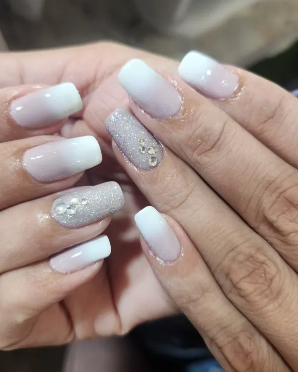 This beautiful ombre manicure blends from a soft nude to a crisp white, with two accent nails fully coated in silver glitter and adorned with rhinestones for extra sparkle.