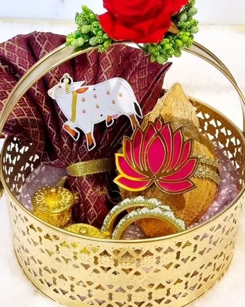This is my signature gold metal basket, a popular choice for weddings and housewarmings. It is filled with auspicious items including a decorated coconut, a rich blouse piece, traditional bangles, and small kumkuma holders, all brought together with beautiful floral and lotus motifs.