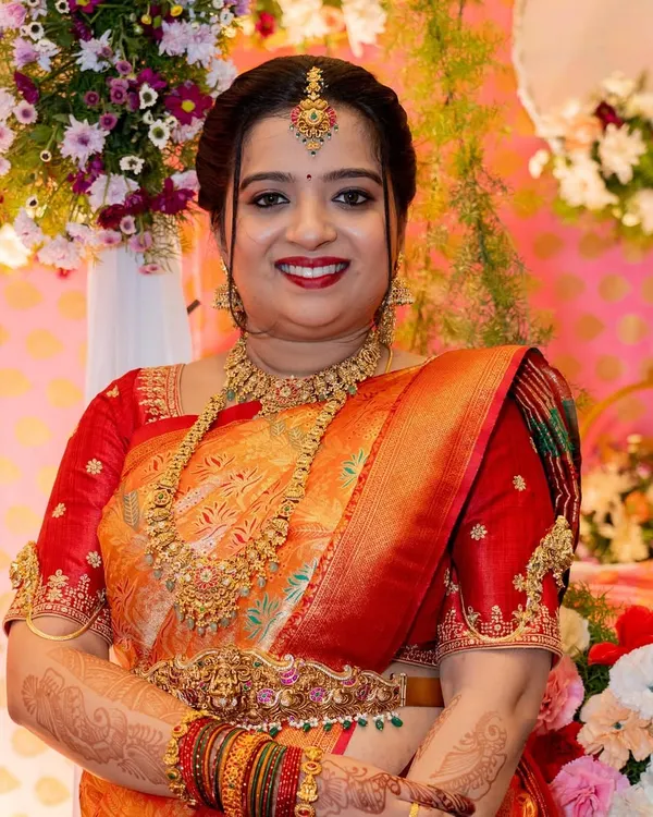 A close-up portrait of Priya for her daughter's naming ceremony. Her makeup is classic and celebratory, with a bright smile and traditional jewelry.