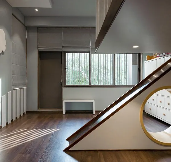This playful kids' room features a custom-built elevated bed with a slide, designed for endless fun. A circular cutout creates a cozy nook beneath, while the cloud-shaped wall light adds a touch of whimsy. The design balances activity with a calming atmosphere.