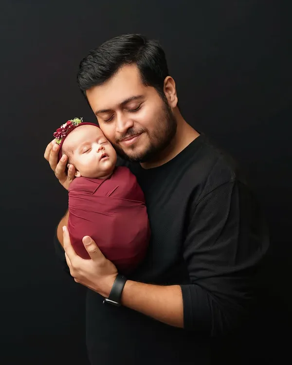 A father holds his swaddled newborn daughter close, a moment of quiet connection. I love capturing these early bonds against a simple, dark background to make the emotion shine.