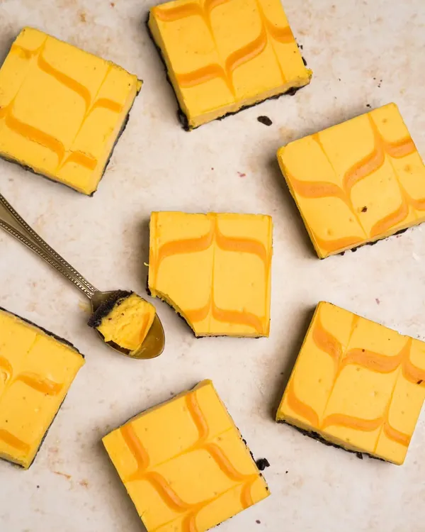 An overhead shot of mango cheesecake bars, creating a beautiful pattern with the swirls. A spoonful is taken out to show the creamy texture.